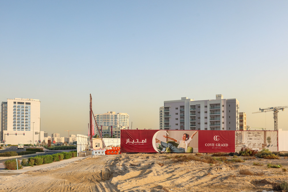Cove Grand By Imtiaz A construction site with a promotional banner for Cove Grand, surrounded by modern buildings and clear sky.