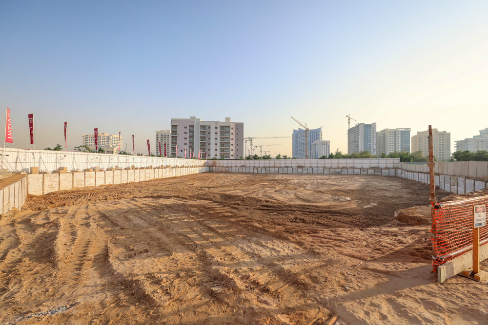 Cove Grand By Imtiaz An open construction site with a circular excavation, surrounded by barriers, urban buildings in the background.