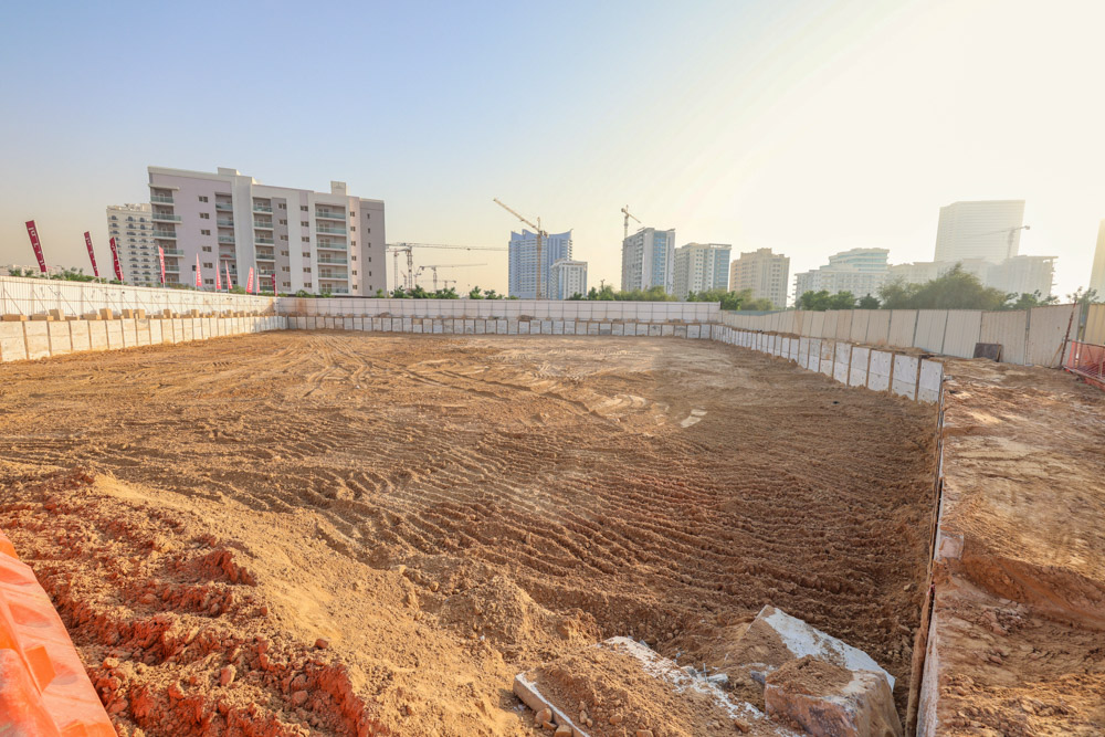 Cove Grand By Imtiaz Cleared construction site with sandy terrain, surrounded by partially built high-rise buildings and fencing.