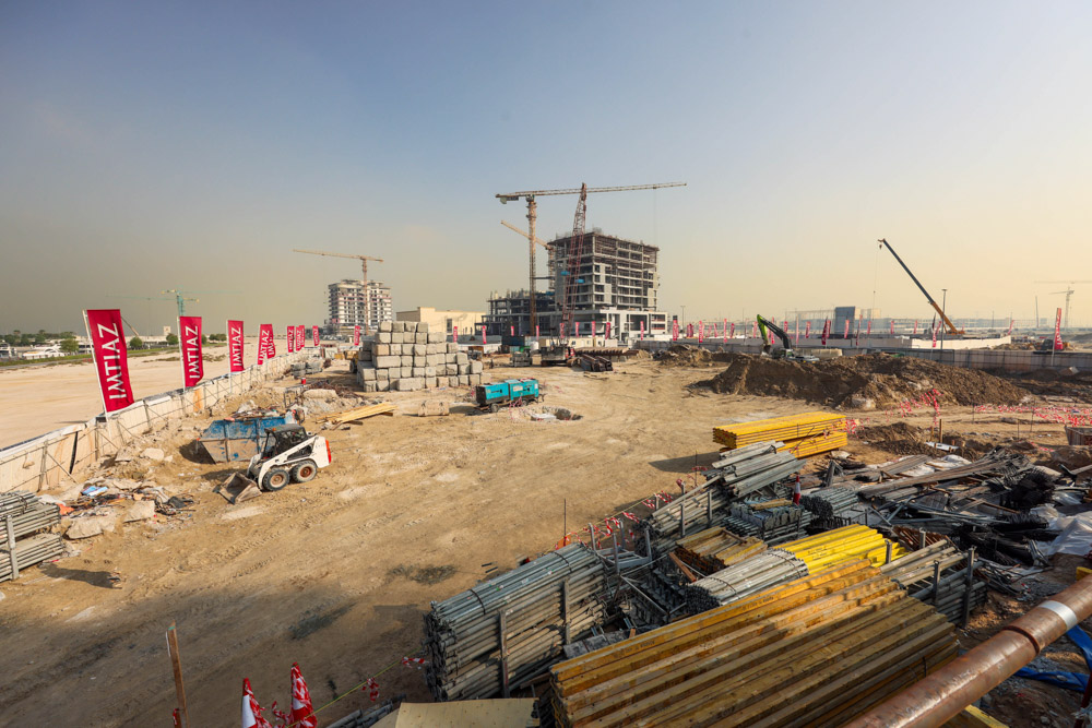 Cotier House 2 By Imtiaz Construction site with heavy machinery, stacks of materials, and cranes against a clear sky, flags visible.