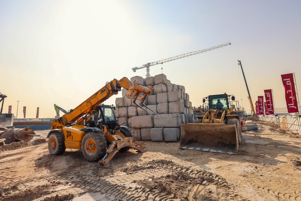 Cotier House 2 By Imtiaz Construction site with heavy machinery, including a loader and telehandler, and stacked concrete blocks.