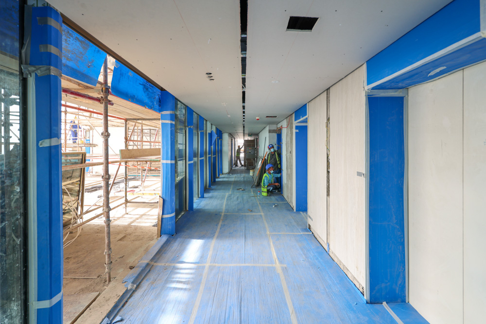Beach Walk Residence A partially constructed hallway featuring scaffolding, blue protective tape, and workers engaged in construction tasks.