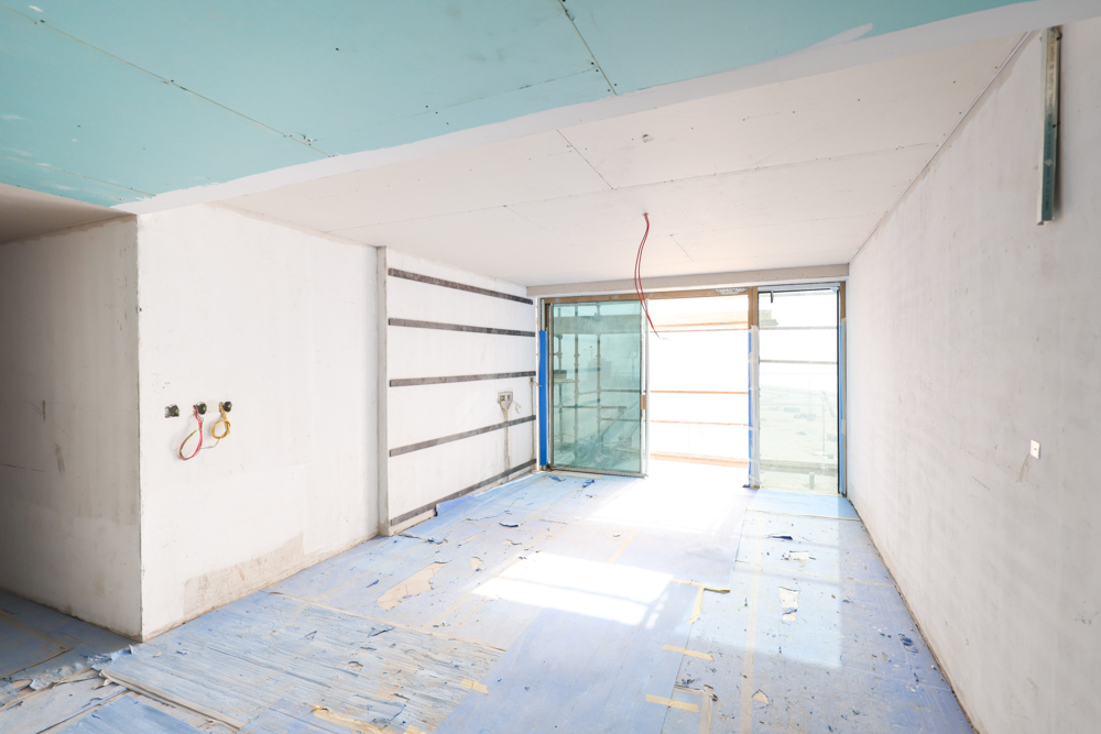 Beach Walk Residence A partially finished room featuring bare walls, a blue floor, and large glass windows under construction.