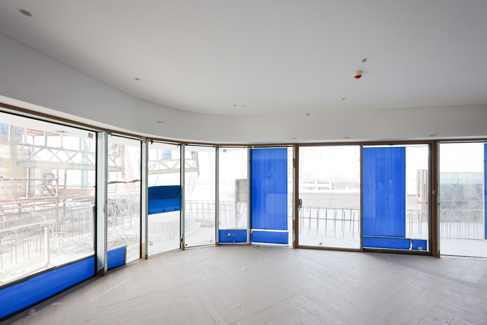 Beach Walk Residence An empty room with large windows covered in blue plastic, showcasing an under-construction view outside.