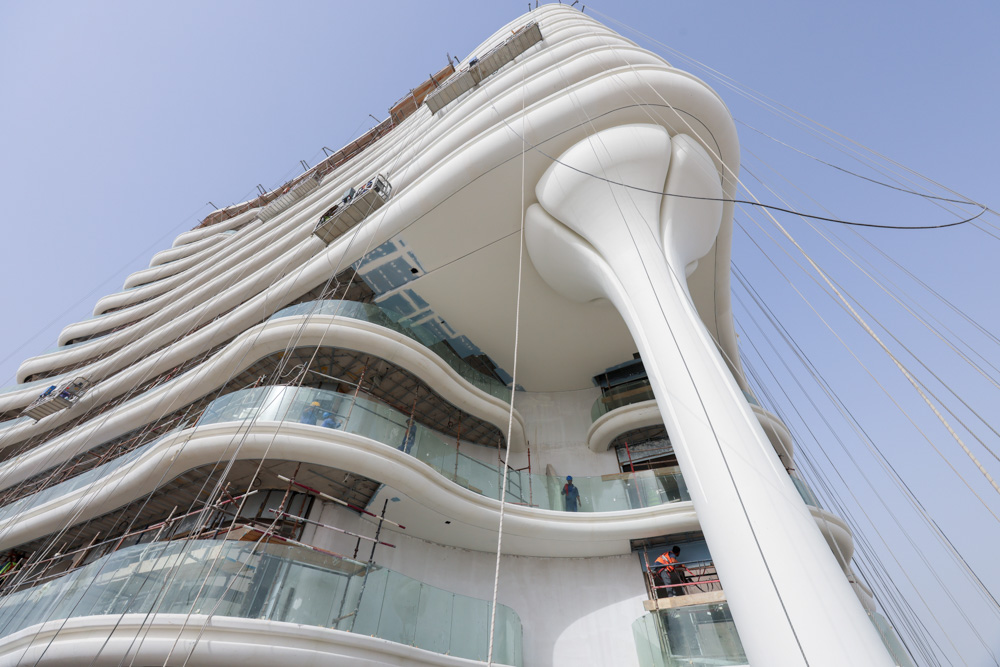 Beach Walk Residence A modern, curvy building under construction with glass balconies and workers visible on the exterior.