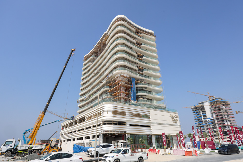 Beach Walk Residence A modern building under construction with a curved facade, surrounded by cranes and parked vehicles.