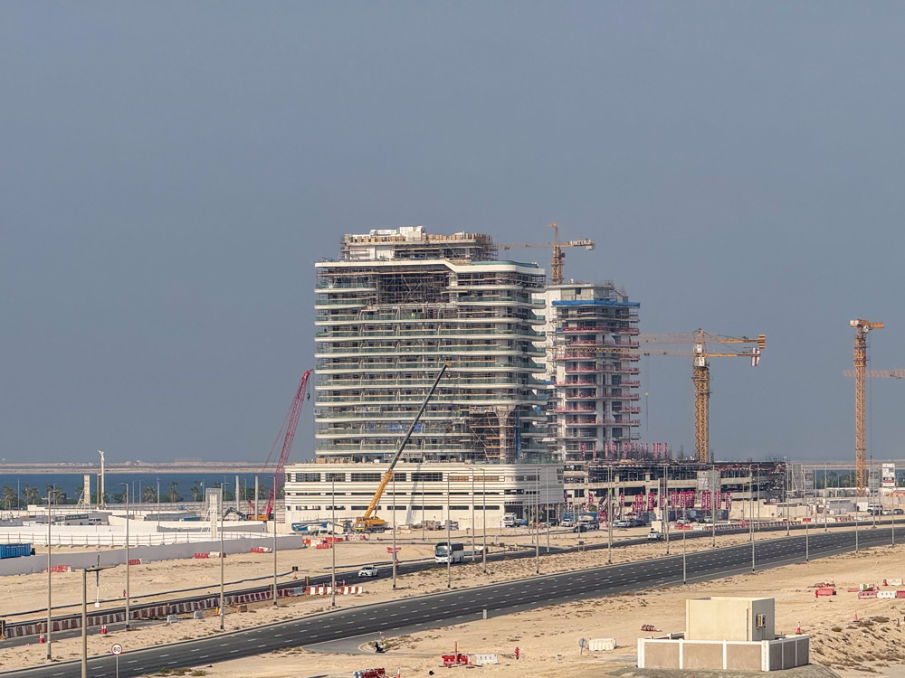 Beach Walk Residence Two partially constructed high-rise buildings with cranes nearby, set against a cloudy sky and sandy terrain.