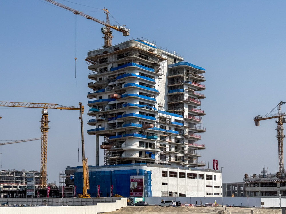 Beach Walk Iii By Imtiaz A partially constructed building with multiple floors, cranes, and scaffolding against a clear sky.