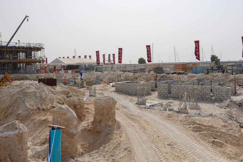 Cotier House 2 By Imtiaz Construction site featuring foundation work, building materials, and workers in a sandy landscape.