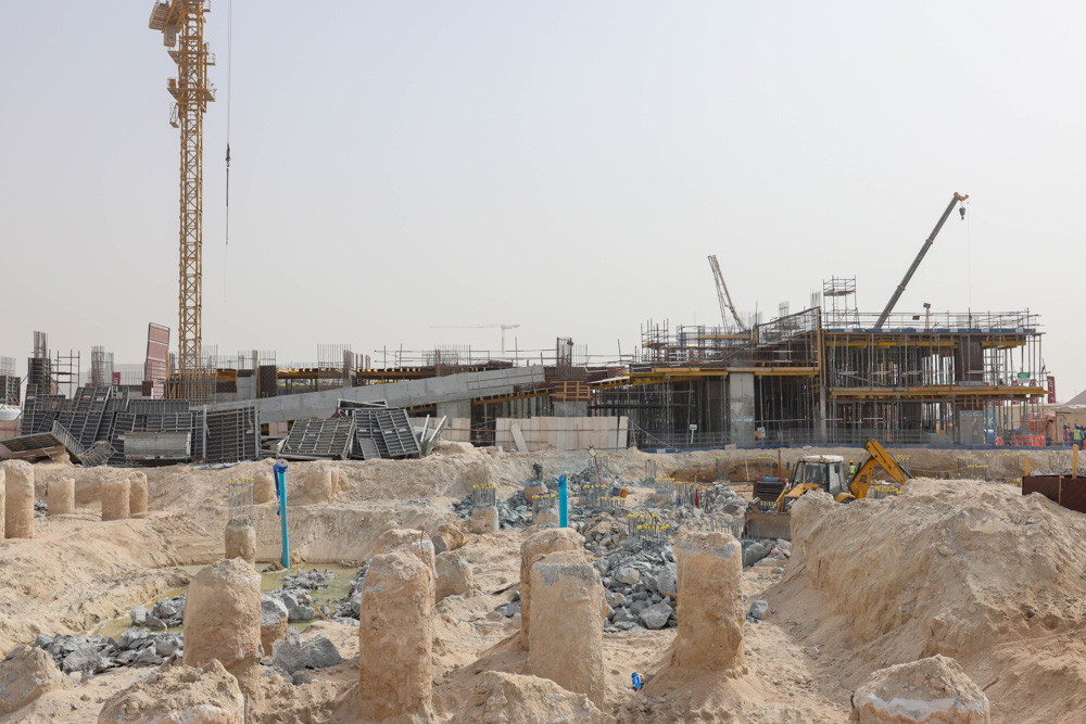 Cotier House 2 By Imtiaz Construction site featuring cranes, scaffolding, and exposed foundations amidst sandy terrain and debris.