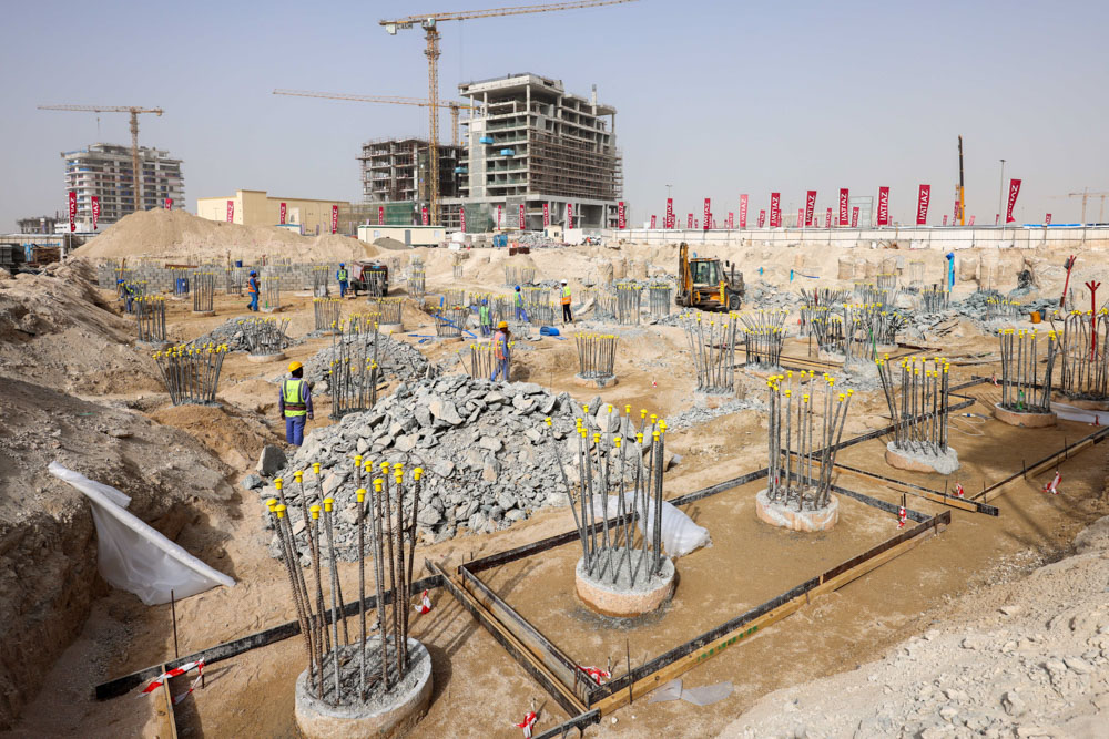 Cotier House 2 By Imtiaz Construction site with scaffolding, workers, concrete foundations, and rebar structures on a sandy terrain.