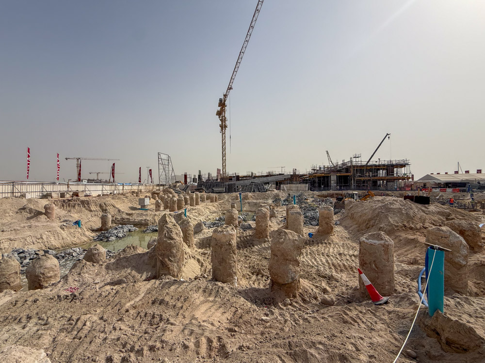 Cotier House 2 By Imtiaz Construction site with excavated ground, visible pillars, machinery, and cranes in the background under a clear sky.