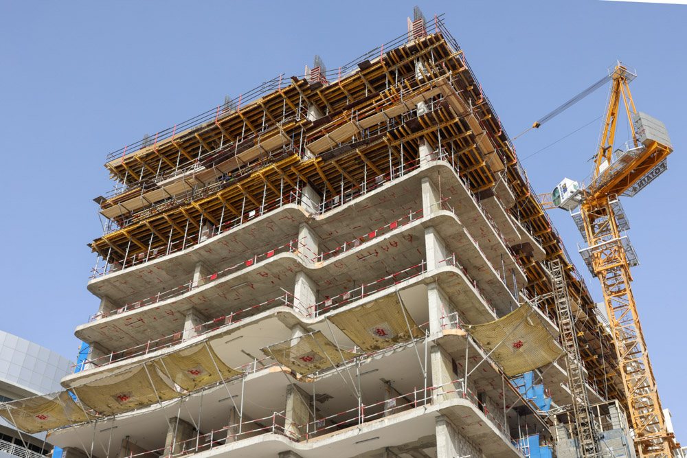 Cove Edition I By Imtiaz 1 A partially constructed building with concrete floors, scaffolding, and a crane against a clear blue sky.