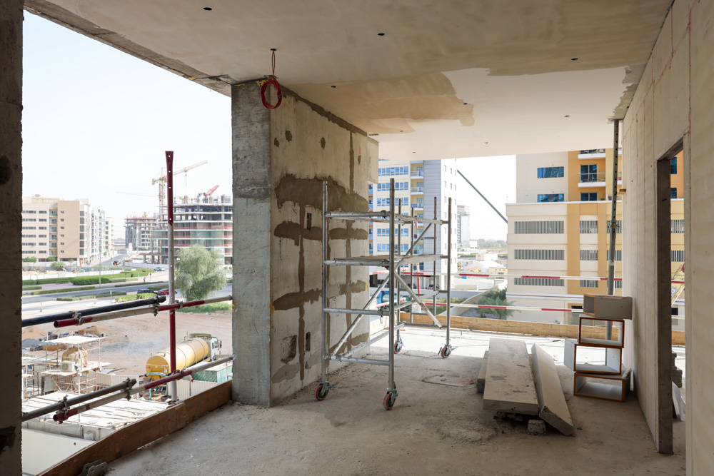 Cove Edition I By Imtiaz 1 Construction site interior showing scaffolding, unfinished walls, and a view of surrounding buildings outside.