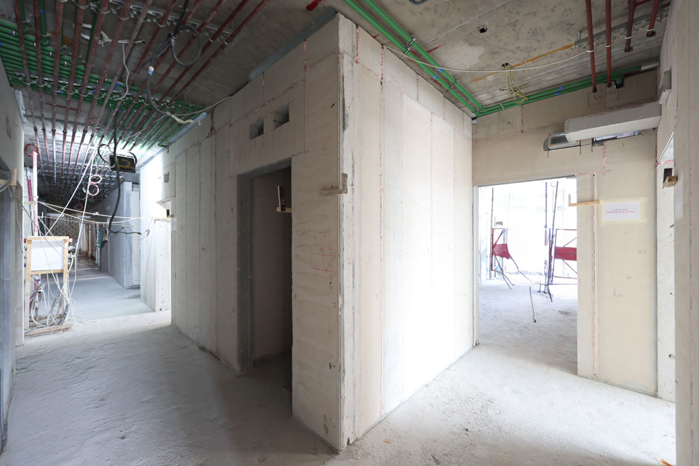 Cove Edition I By Imtiaz 1 A partially constructed interior hallway with exposed walls, colorful pipes, and scaffolding visible through openings.