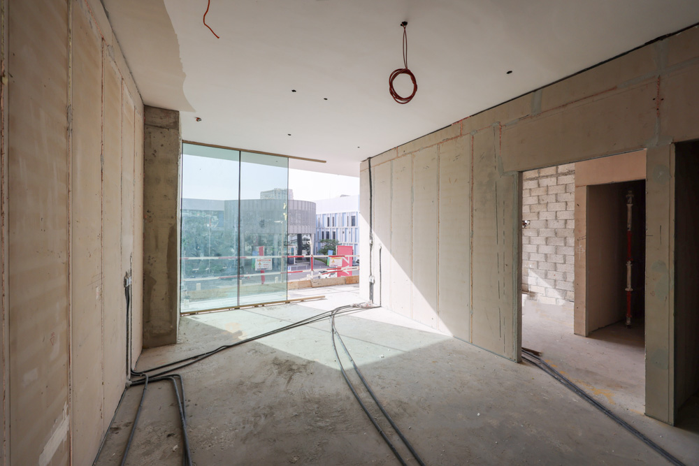 Cove Edition I By Imtiaz 1 An unfinished, spacious interior room featuring large glass windows and exposed construction elements on the walls.