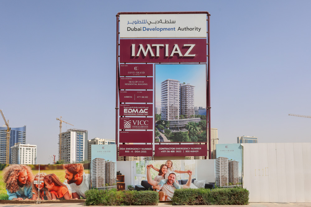 Cove Grand By Imtiaz A construction sign featuring an architectural rendering, project details, and images of happy families enjoying life.