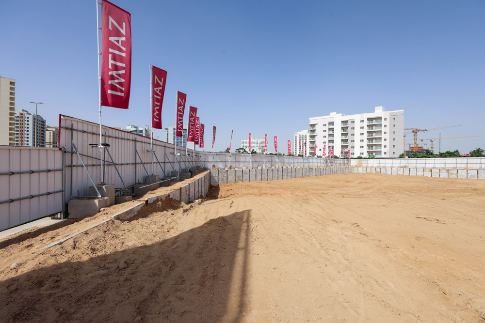 Cove Grand By Imtiaz A construction site featuring sandy ground, banners, and adjacent buildings under a clear blue sky.