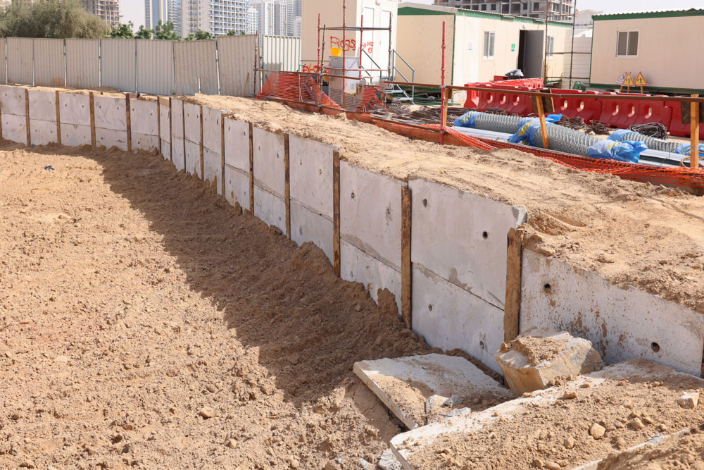 Cove Grand By Imtiaz Construction site with concrete wall segments, sandy ground, and equipment in the background under a clear sky.