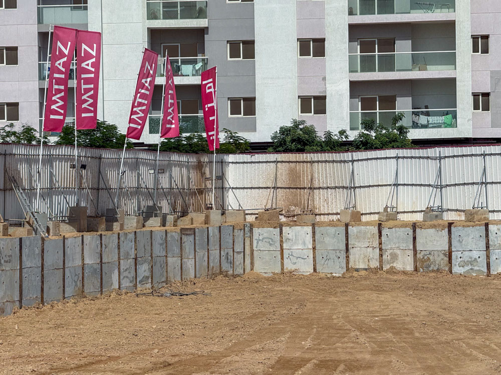 Cove Grand By Imtiaz Construction site with concrete barriers and several flags displaying "Imtiaz" against a backdrop of buildings.
