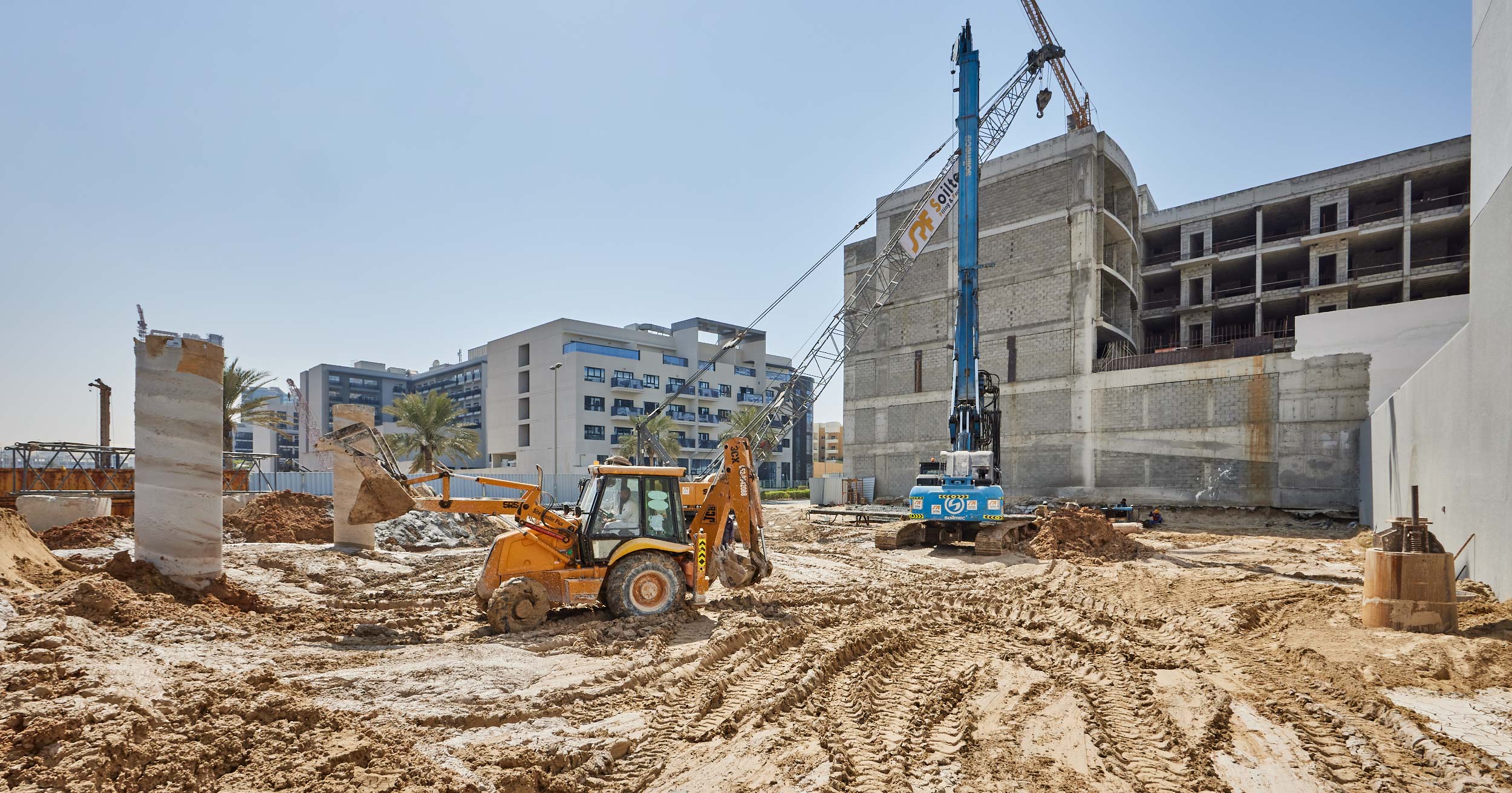 Pearl House By Imtiaz Construction site with machinery, including a backhoe and crane, amidst piles of dirt and unfinished buildings.