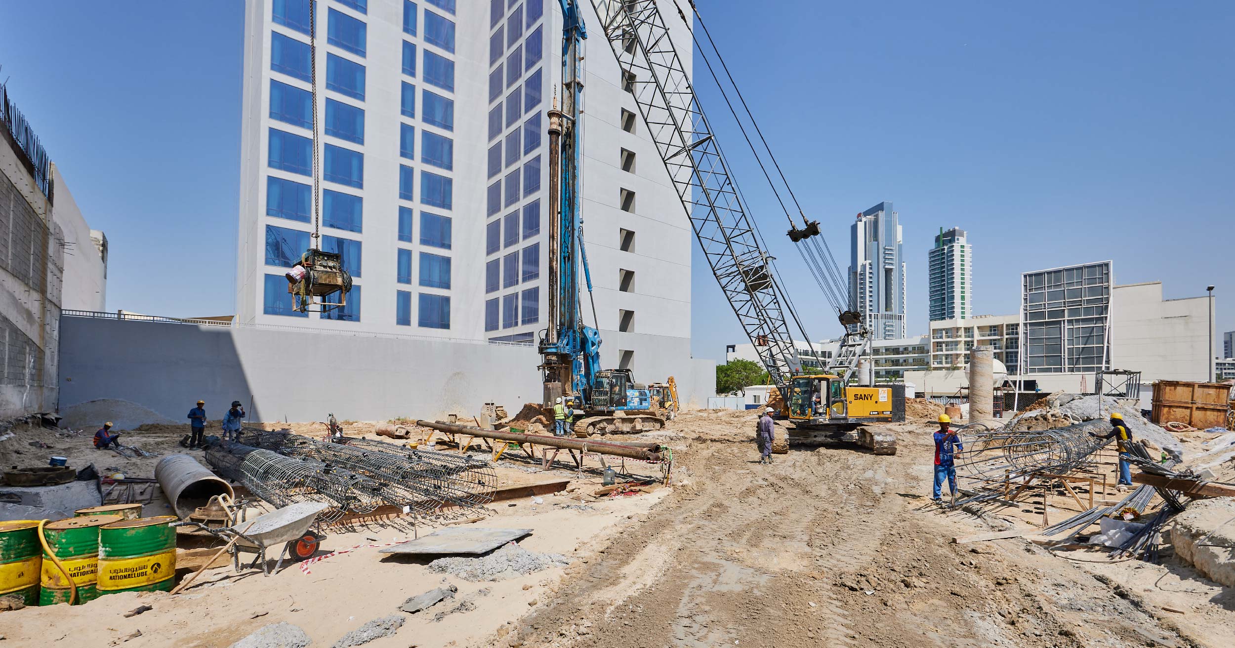 Pearl House By Imtiaz Construction site with workers, heavy machinery, and a modern building under development against a clear sky.
