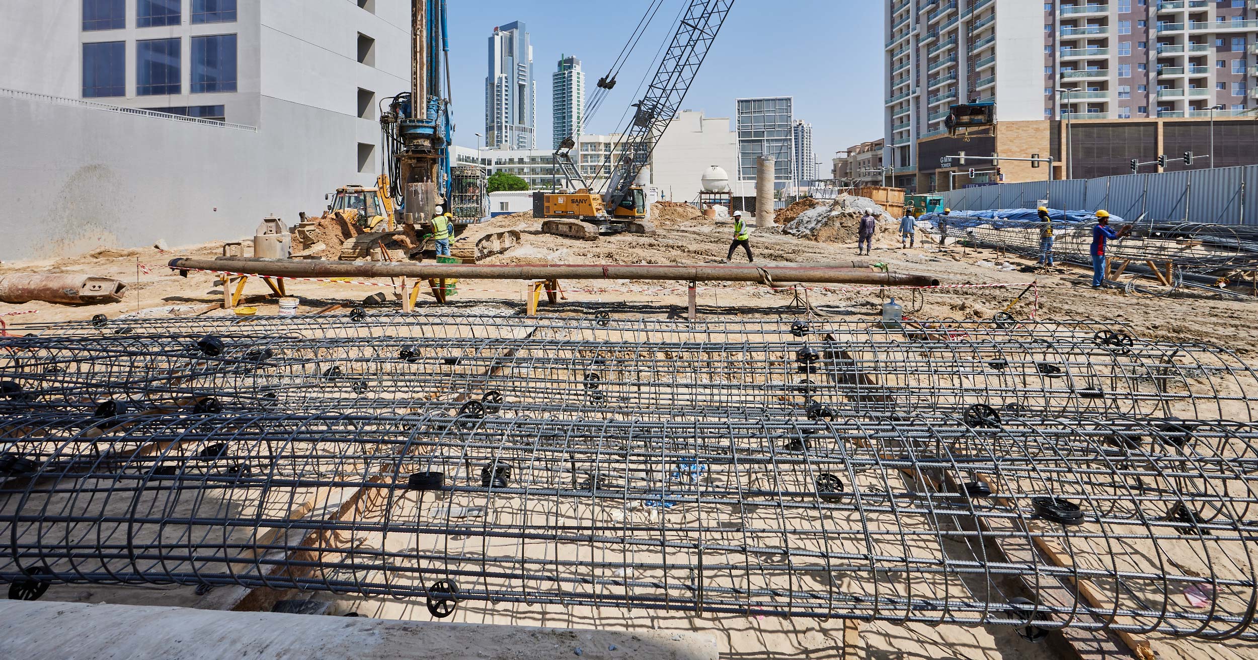 Pearl House By Imtiaz Construction site featuring workers, heavy machinery, and steel reinforcement bars laid out on the ground.
