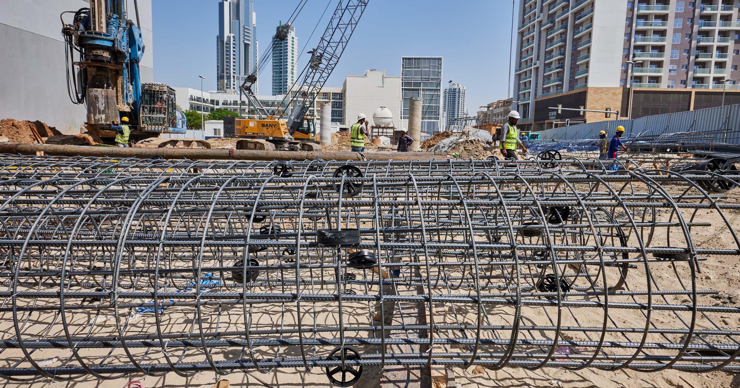 Pearl House By Imtiaz Construction site featuring workers, machinery, and steel rebar structures against a backdrop of buildings and cranes.