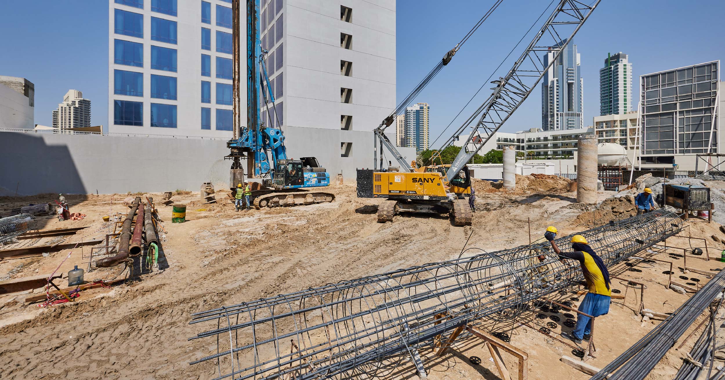 Pearl House By Imtiaz Construction site featuring machinery, workers, and building materials under a clear blue sky.