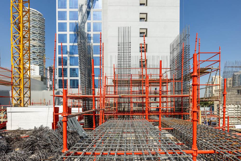 Pearl House By Imtiaz A construction site featuring steel rebar and bright orange scaffolding with buildings in the background.