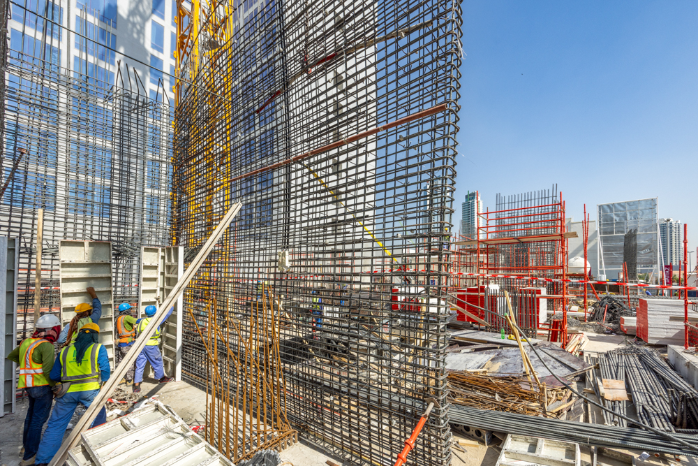Pearl House By Imtiaz Construction site with workers, scaffolding, and materials, showcasing a building framework under blue sky.