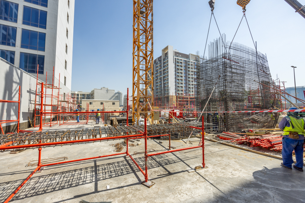 Pearl House By Imtiaz Construction site featuring scaffolding, cranes, workers, and steel reinforcements against a clear blue sky.