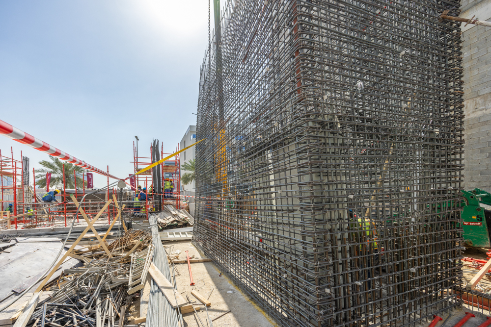 Pearl House By Imtiaz Construction site featuring a scaffolding structure, rebar framework, and workers in safety gear under a clear sky.